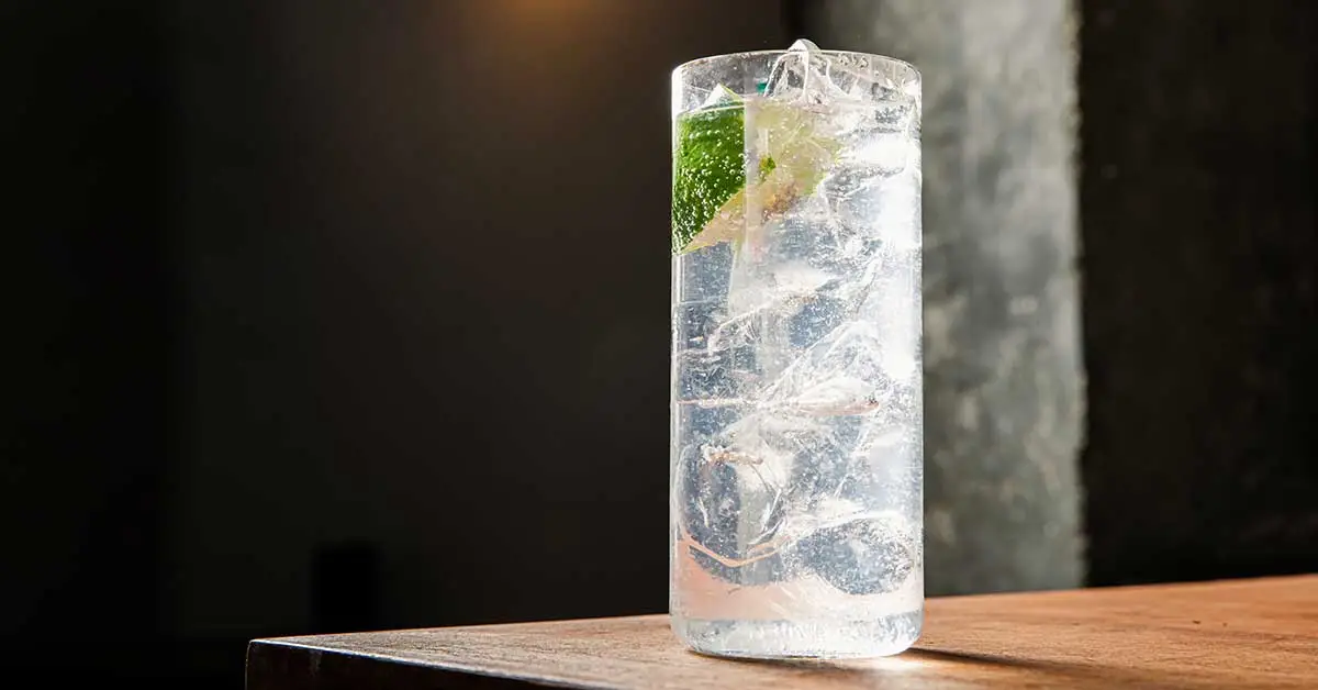 A tall, slim highball glass packed with ice and a wedge of lime.