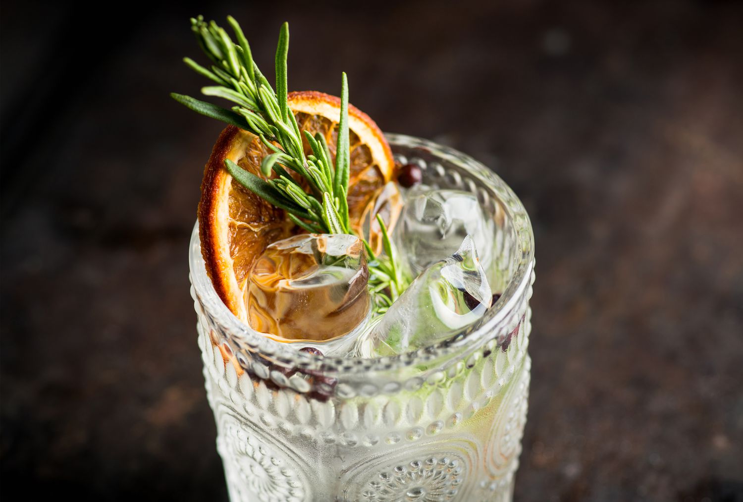 A textured highball glass with rosemary sprigs, dried orange, and clear ice.